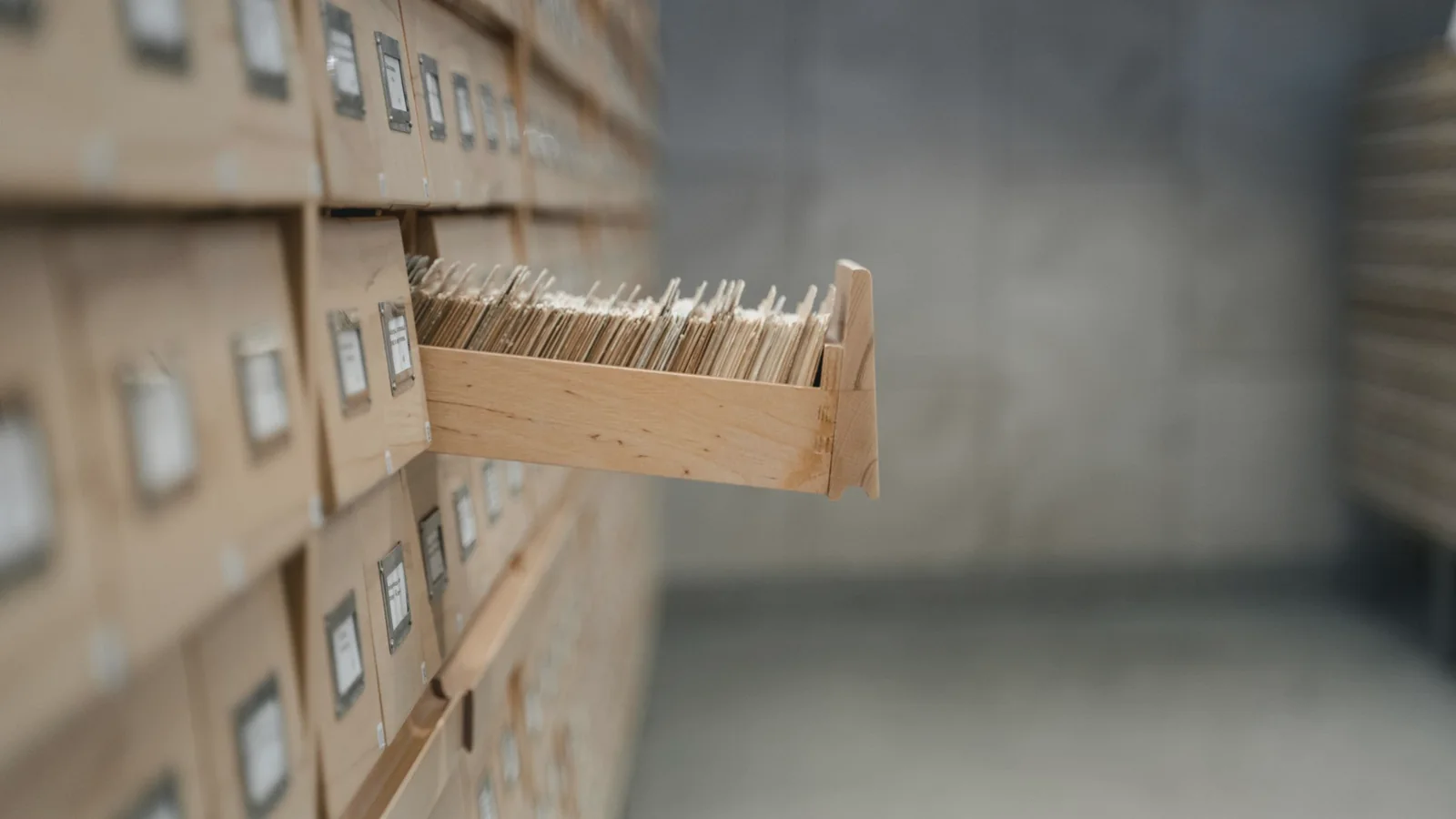 Ein Holzschrank mit vielen kleinen Schubladen, eine Schublade ist geöffnet und zeigt aufrecht stehende Karteikarten.