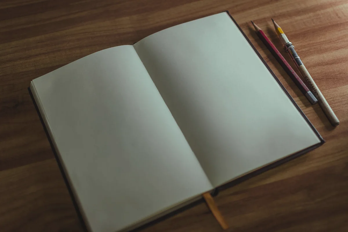 Aufgeschlagenes leeres Notizbuch mit zwei Bleistiften auf einem Holztisch.