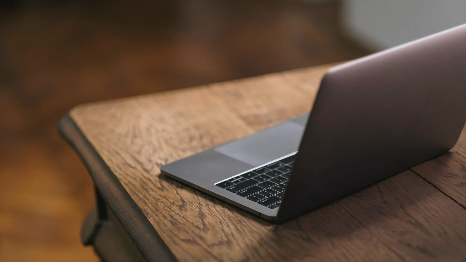 Aufgeklappter Laptop von hinten auf einem dunklen Holztisch, der Bildschirm ist nicht zu sehen.