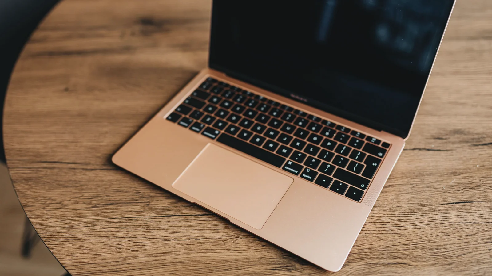 Aufgeklappter Laptop auf einem runden Holztisch von schräg oben.